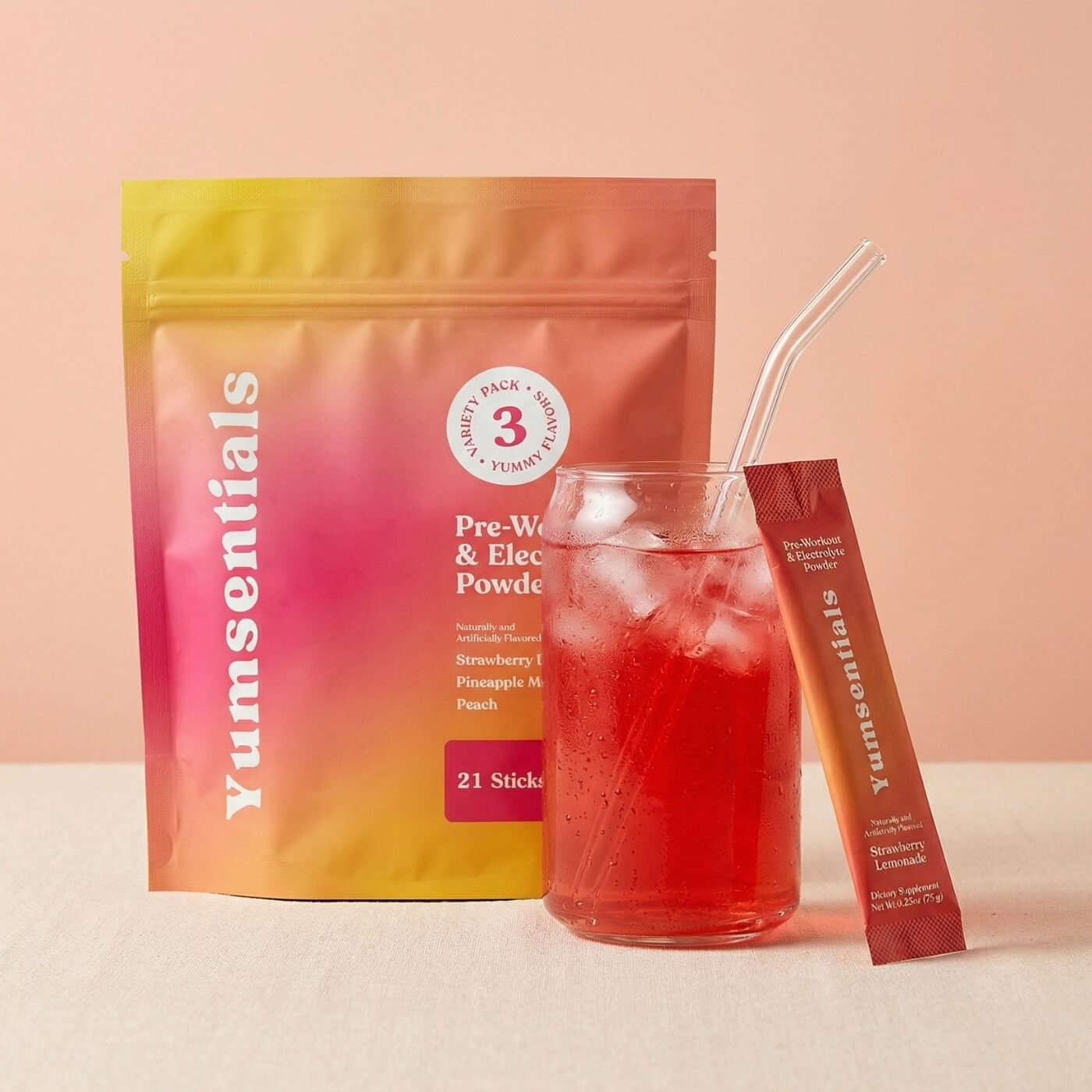 Yumsentials pre-workout and electrolyte powder package with a glass of red drink and straw on a peach background